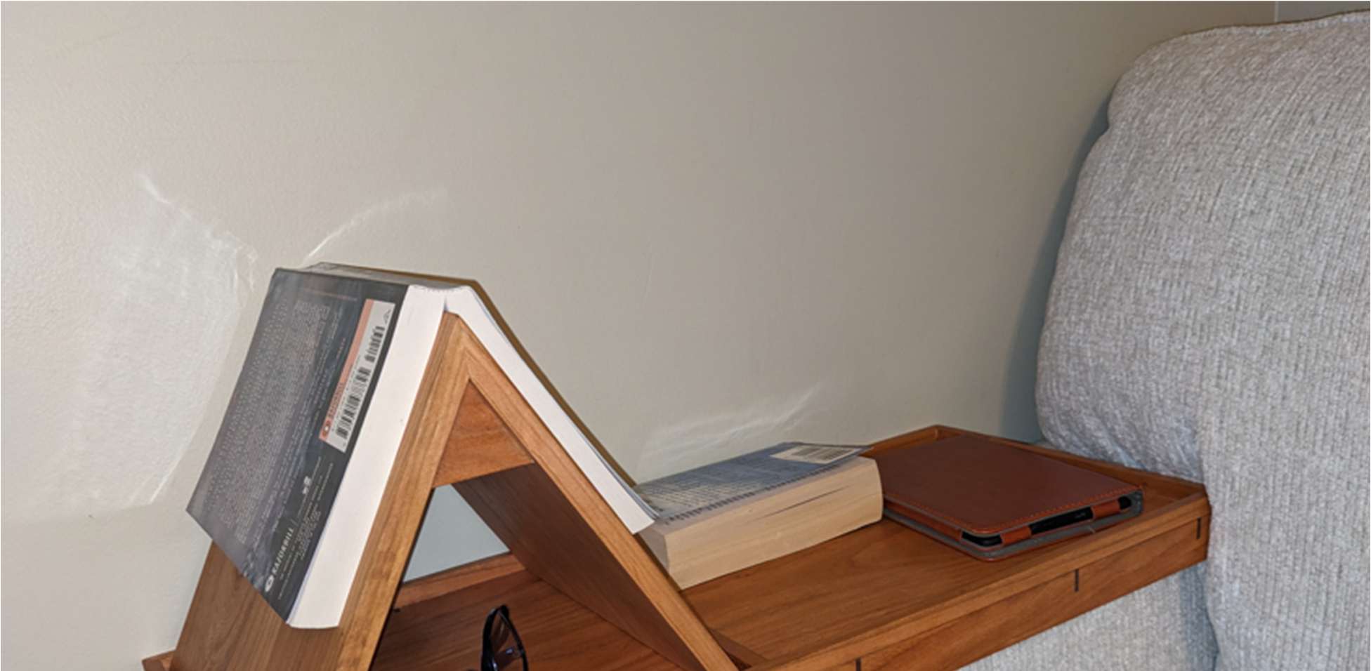 Solid cherry armrest book valet fitted to a couch arm, holding a book, glasses, and a tablet.