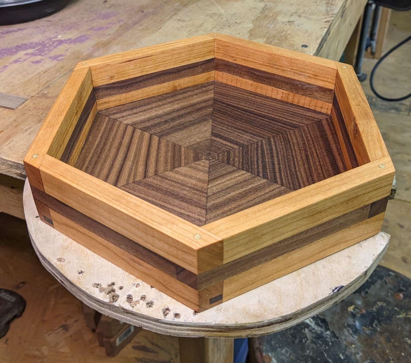 Finished hexagonal tray in alternating walnut and cherry with a centered starburst base pattern and exposed brass joinery pins.