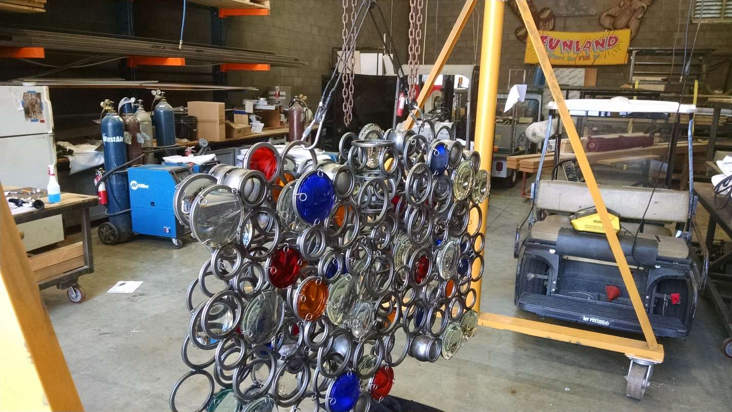 Intricate welded steel ring grid matrix suspended overhead, set with colored glass lens inserts.