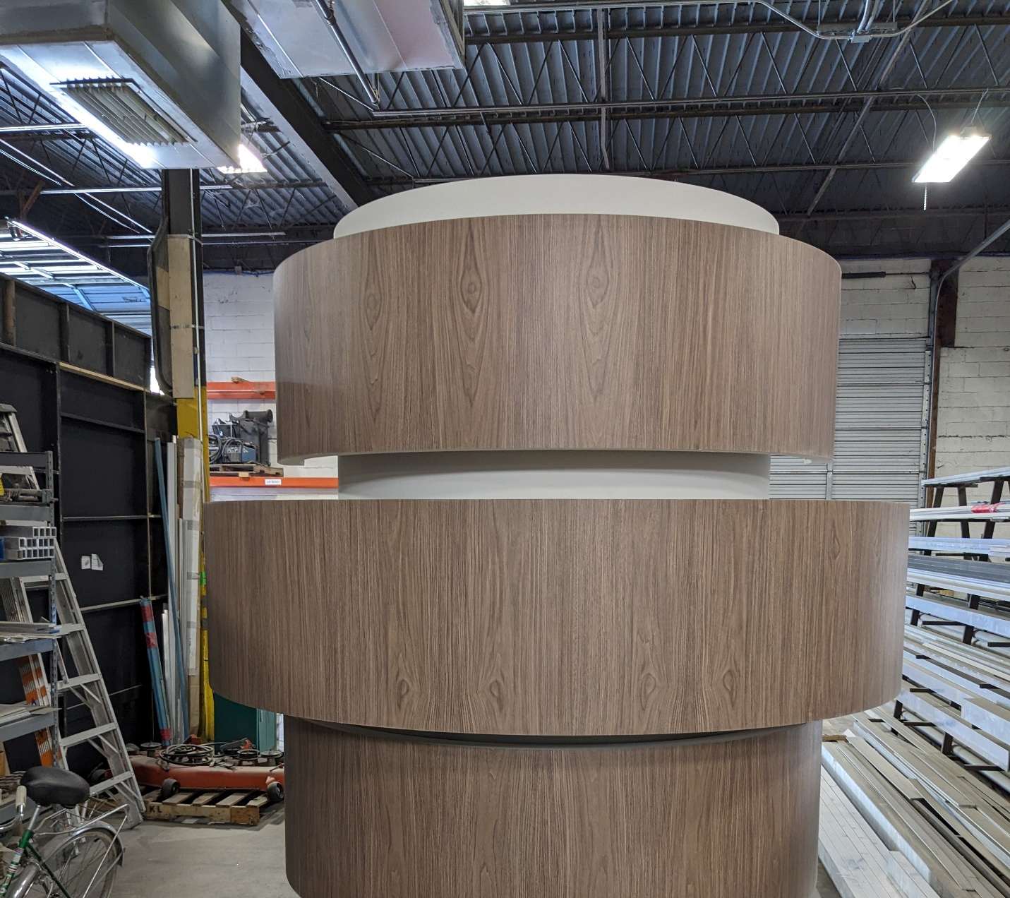Completed multi-tiered cylindrical display tower finished in walnut wood-grain veneer with a white laminate base.